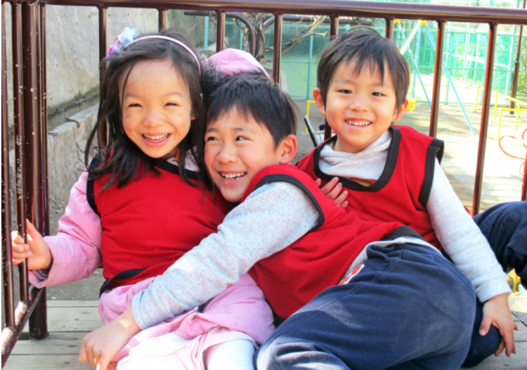 Three children smiling and hugging on a playground, showing friendship and emotional connection