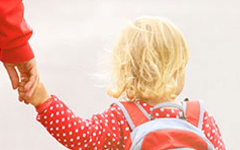 Toddler walking with a caregiver, wearing a backpack, symbolizing early learning journeys