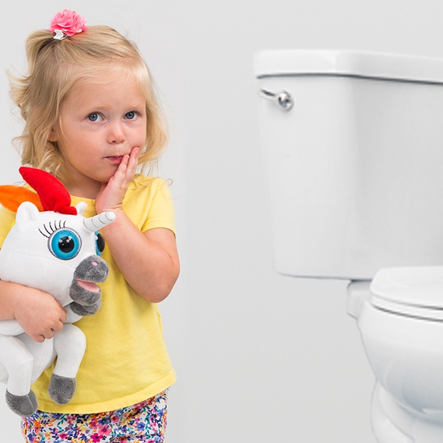 Young child holding a plush unicorn near a toilet, representing gentle and supportive approaches to toilet training.