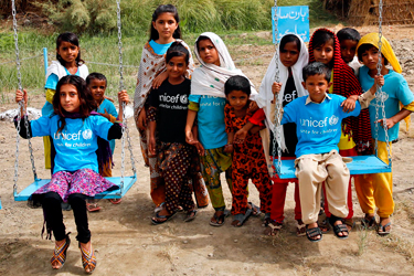 Children wearing UNICEF shirts on swings and posing together, representing global child welfare