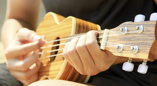 Person playing a ukulele in natural light, showcasing creative expression