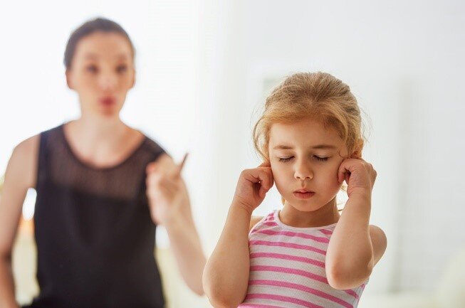 Child plugging ears while adult speaks, symbolizing emotional sensitivity