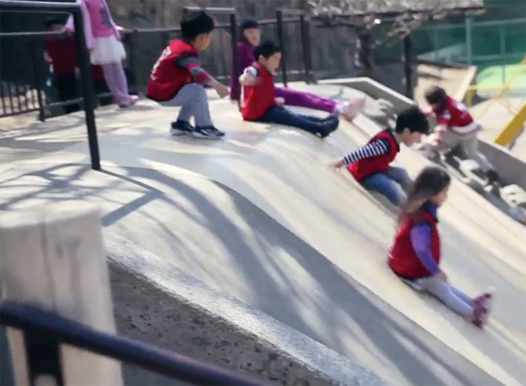 Children sliding down a large outdoor structure in coordinated red vests, showcasing joyful and active learning at Ohana International School.