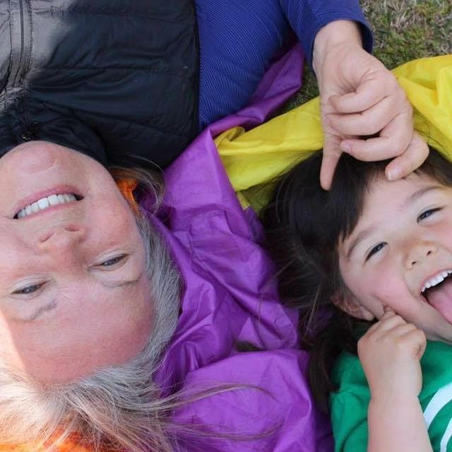 Smiling adult and child laying on colorful parachute cloth, representing joyful connection, care, and community at Today We Dream.